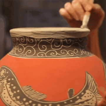 Deb Kuzyk decorating a large vase with fish pattern